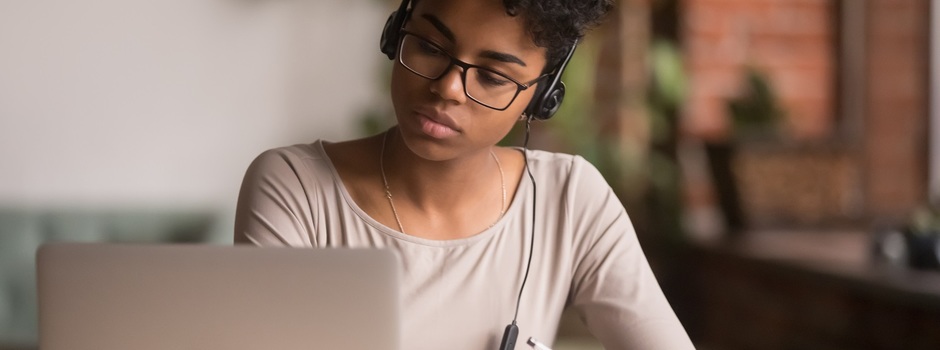 Focused mixed race woman wearing headphones watching webinar write notes