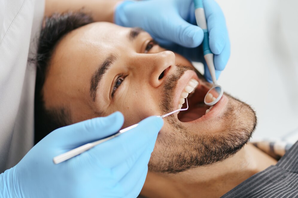 jovem-sorridente-sentado-na-cadeira-do-dentista-enquanto-o-medico-examina-os-dentes_158595-7733
